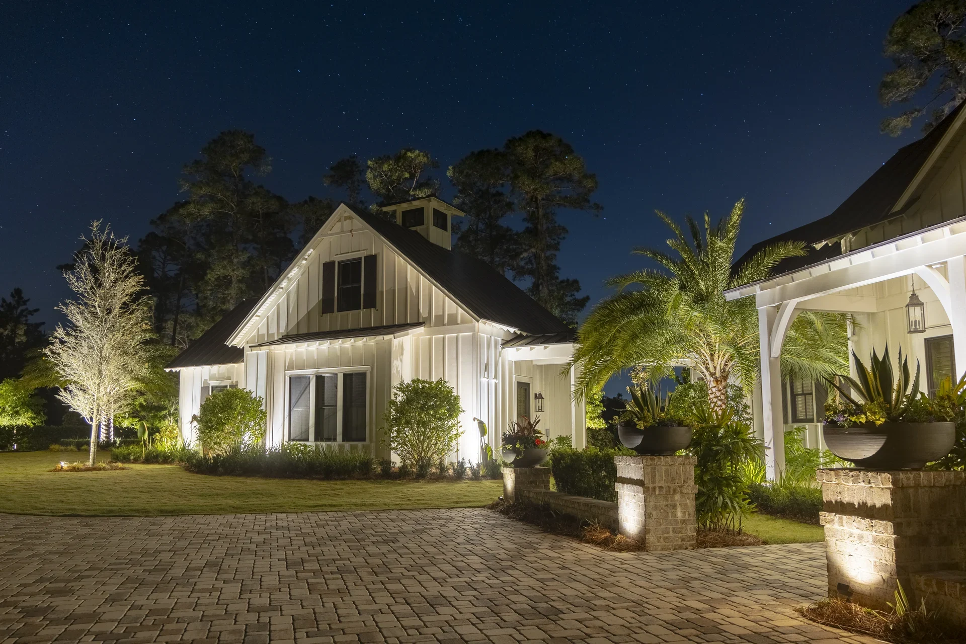 Landscape lights highlighting palms and a home beside a brick drive