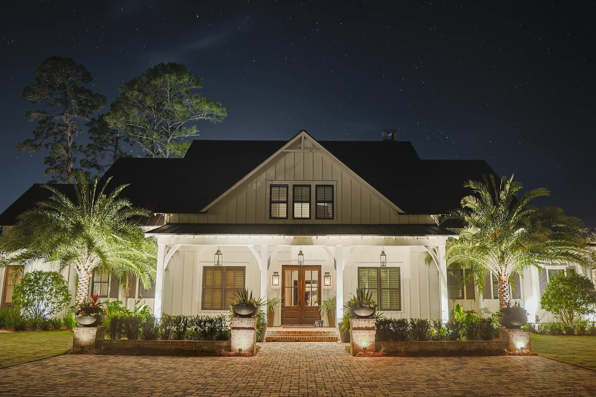 A warmly illuminated front porch framed by palms and garden planting