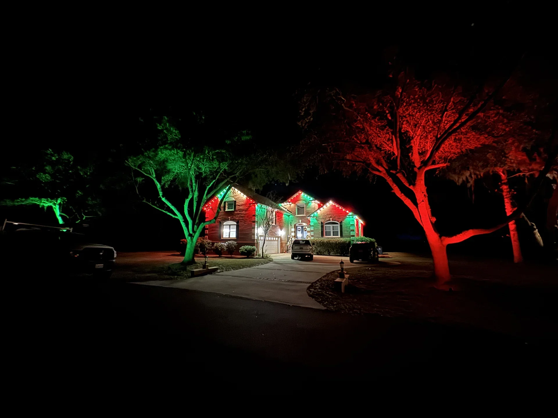 A home framed by trees illuminated in Christmas red and green