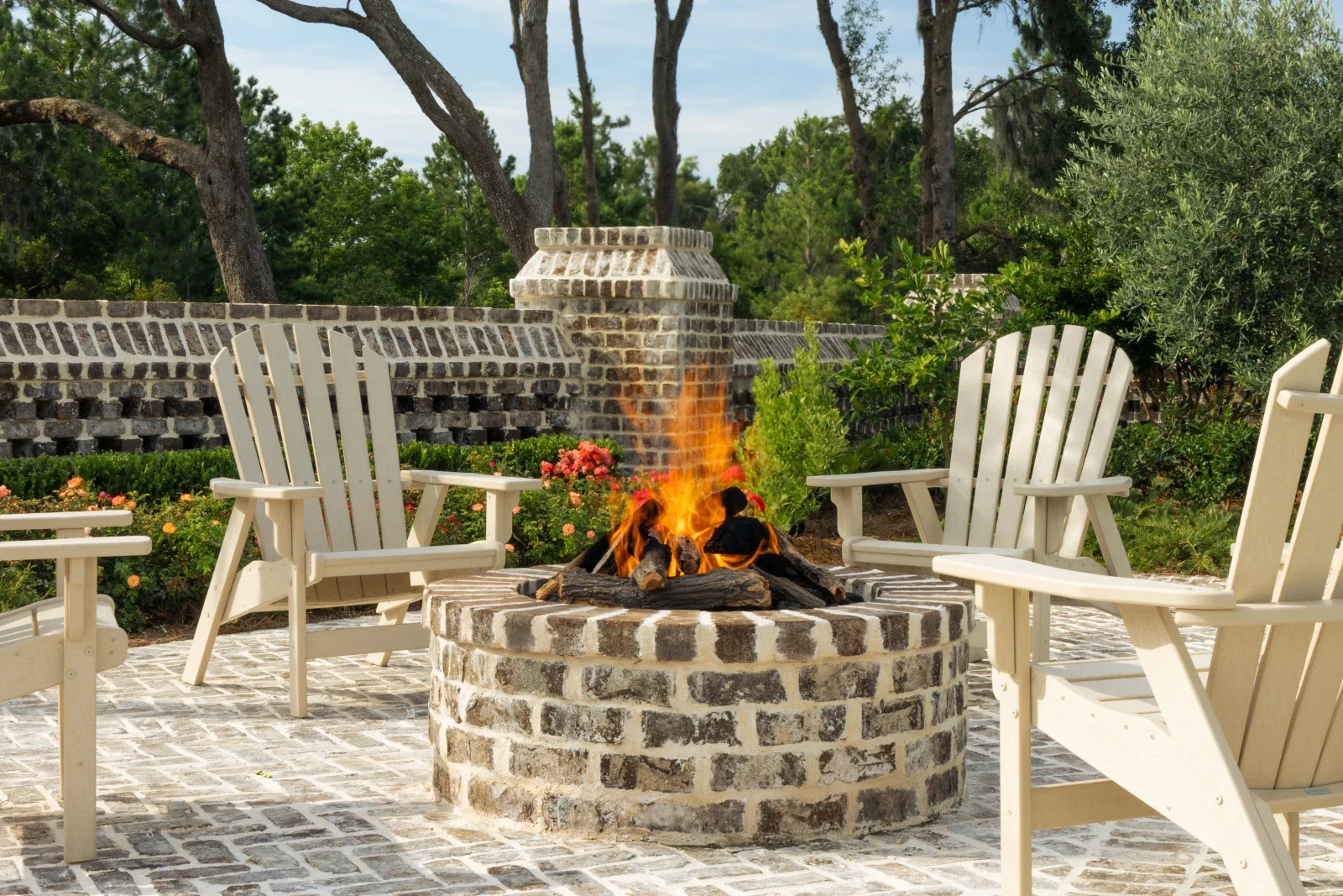 Stone fire pit with Adirondack chairs beneath mature trees